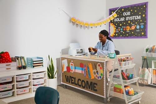 Teacher at welcome desk in classroom with educational decor.