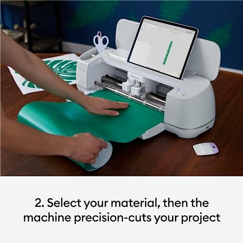 Person using a cutting machine with a green material and tablet screen.