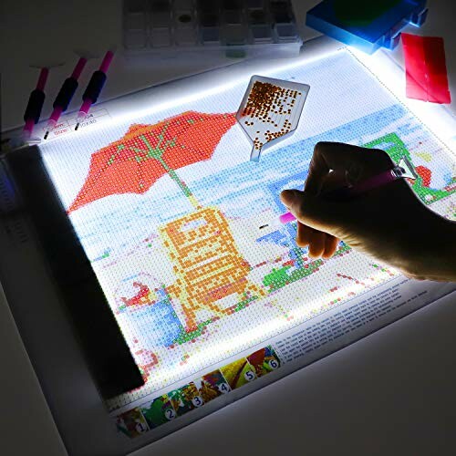 Person using a diamond painting kit on a light pad.