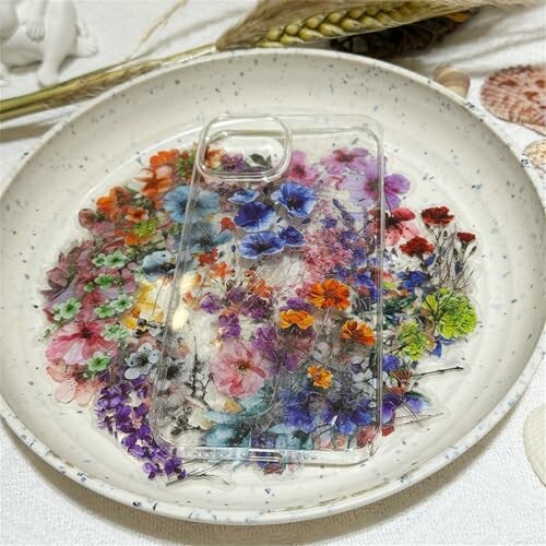 Clear phone case with colorful pressed flowers on a ceramic plate.