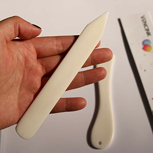Person holding a bone folder tool for crafting.