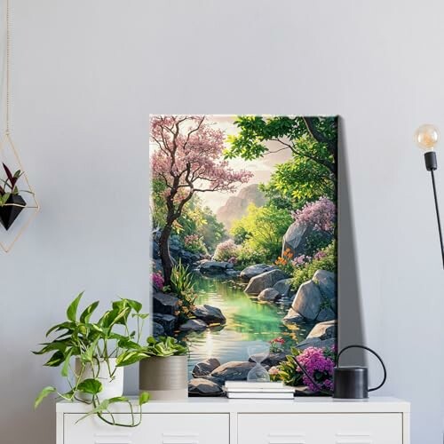 Nature wall art depicting a serene river scene with trees and rocks, placed on a shelf with plants and a lamp.
