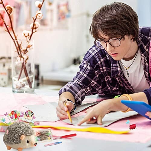 Person drawing on a desk with a hedgehog figurine and stationery.